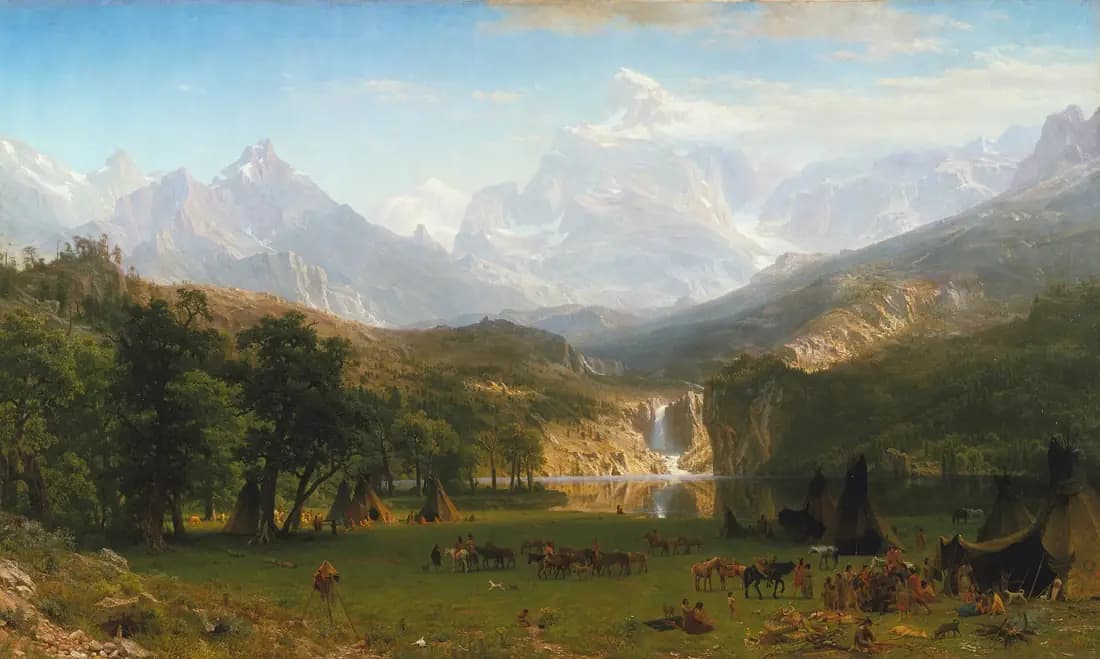 Sunlit Rocky Mountain peaks rise above a lake, waterfall and Shoshone encampment