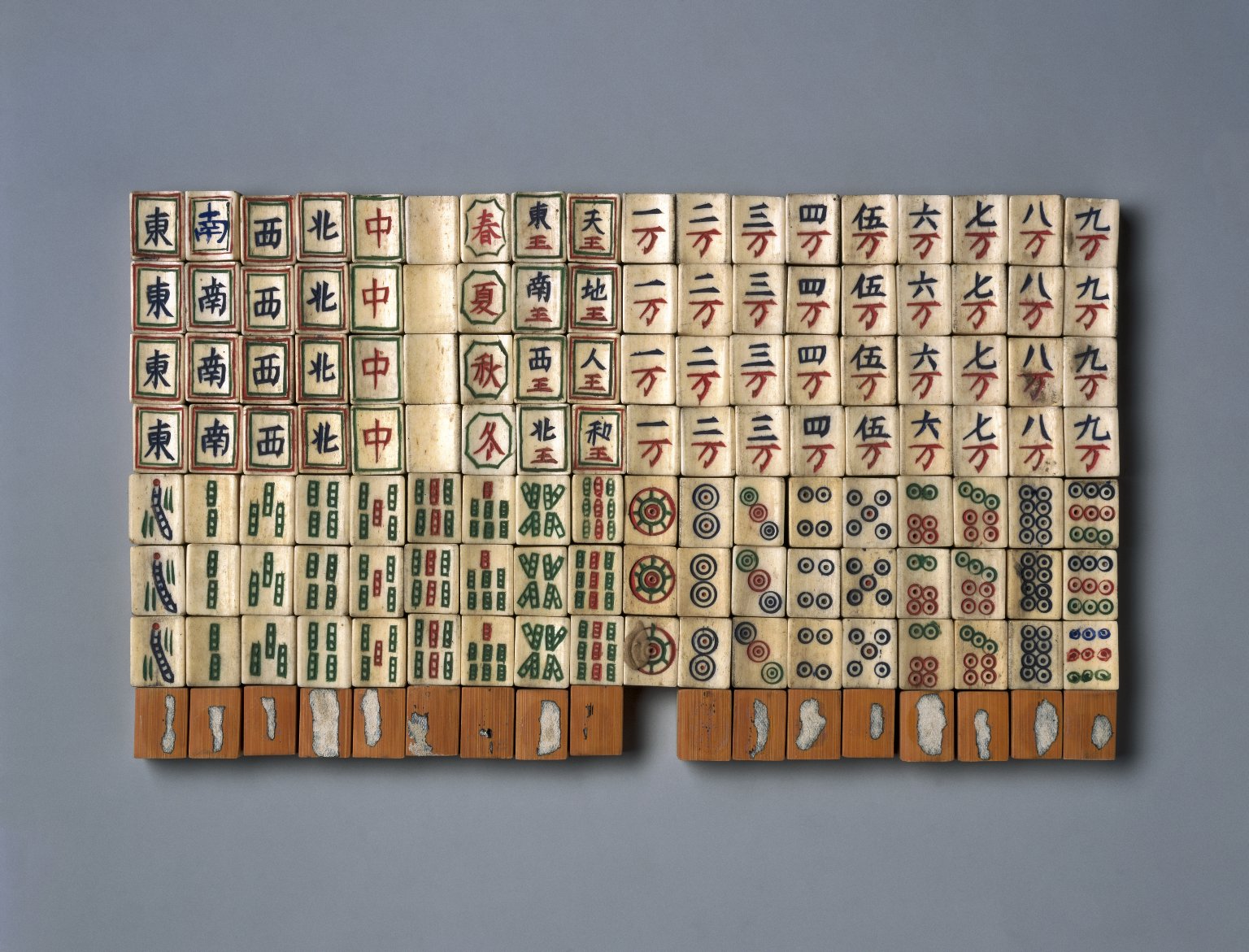 Late-19th-century Chinese bone-and-bamboo mahjong tiles arranged in rows, with circles, bamboo, characters and other engraved symbols.
